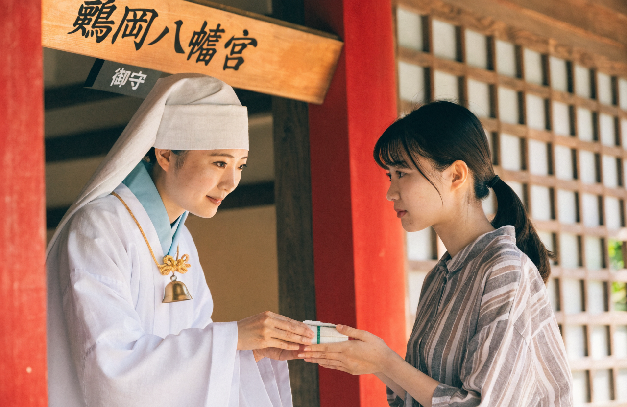 鶴岡八幡宮の授与所の前で、巫女装束の女性スタッフがお守りを丁寧に手渡している場面